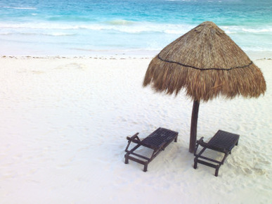 A Palm Frond Umbrella and Two Chairs on a White Sand Beach